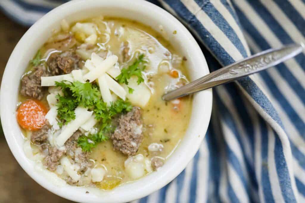 overview shot of cheeseburger soup in a white bowl topped with parsley and cheese with a blue and white bowl to the right.