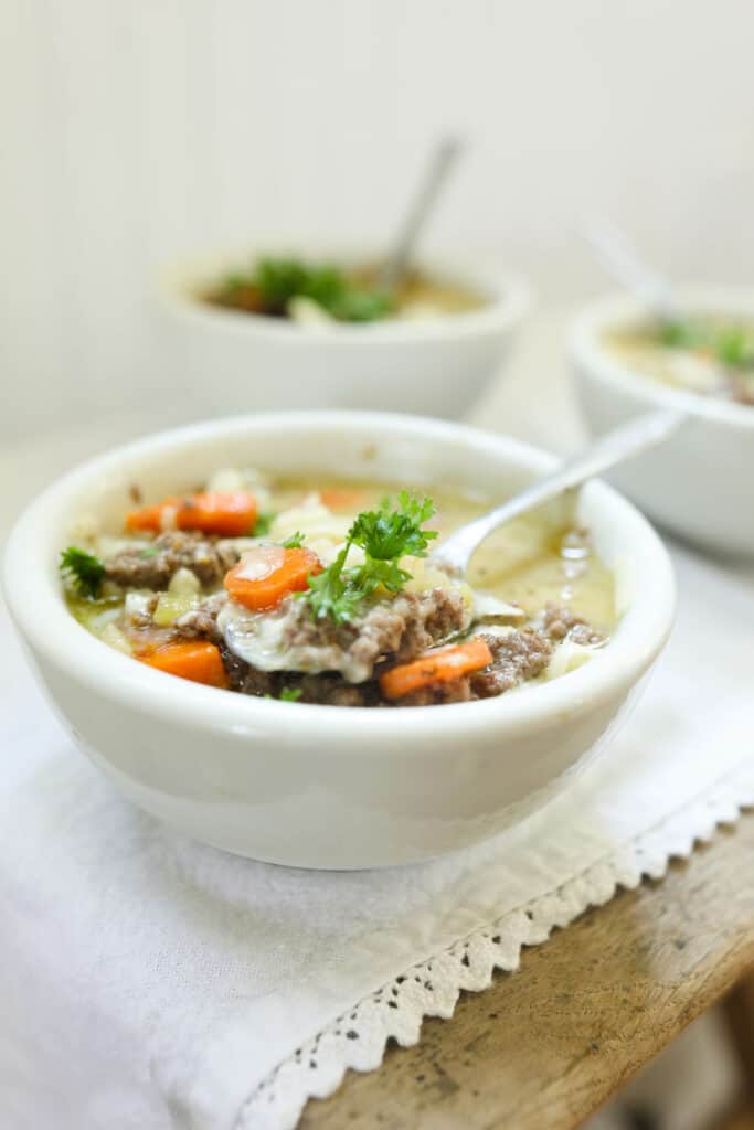 three bowls on cheeseburger soup in white bowls on a white laced table runner