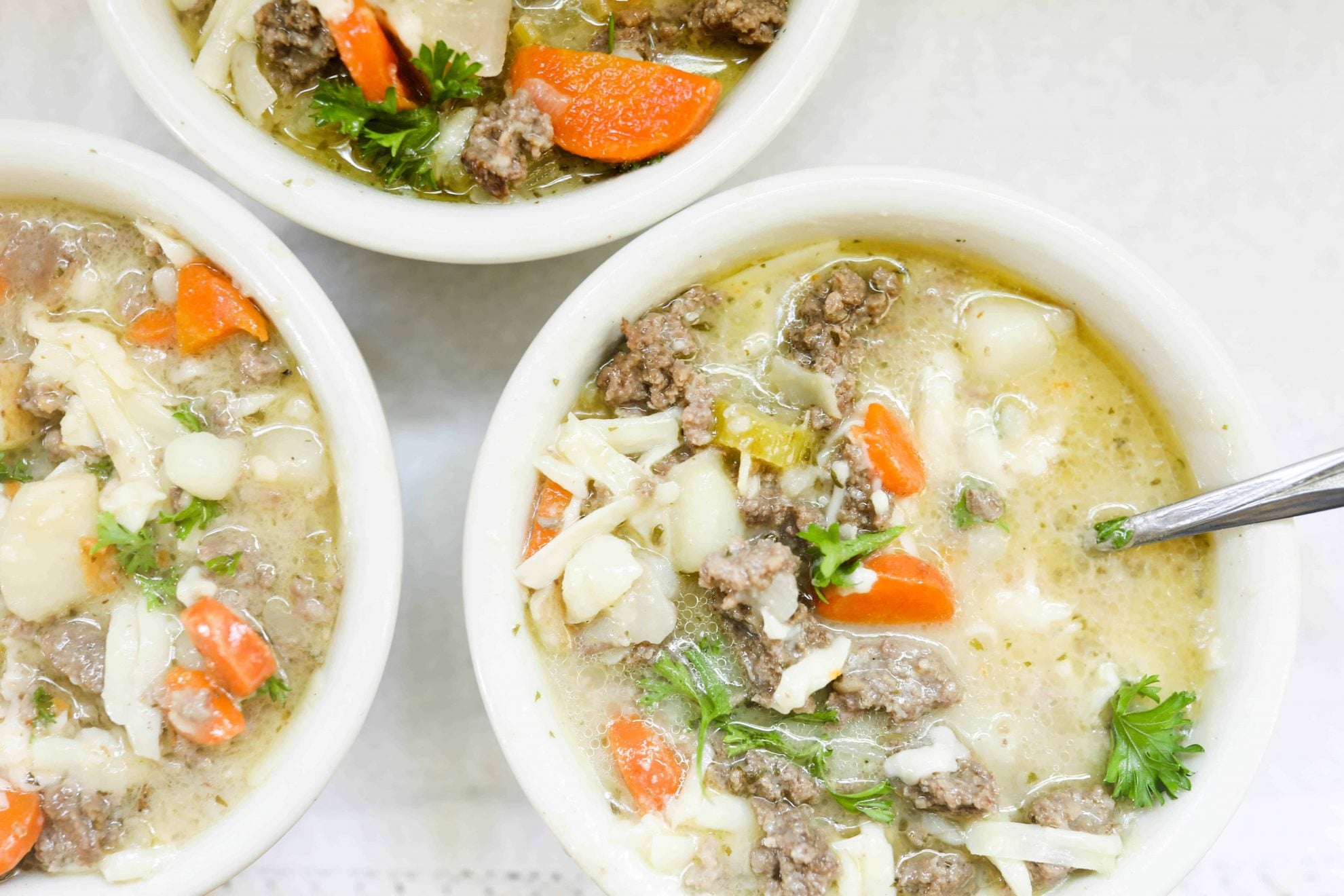 A soup pot filled with potatoes, ground beef, carrots, and bone broth simmering on the stove.