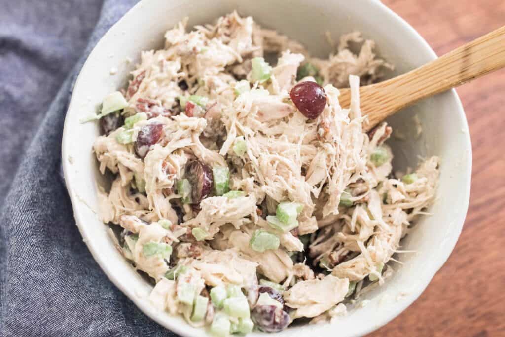 Classic chicken Salad with grapes in a white bowl with a wooden spoon on top a blue towel