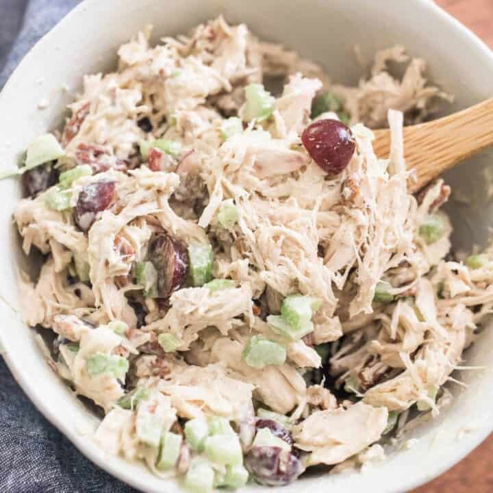 Classic chicken Salad with grapes in a white bowl with a wooden spoon on top a blue towel