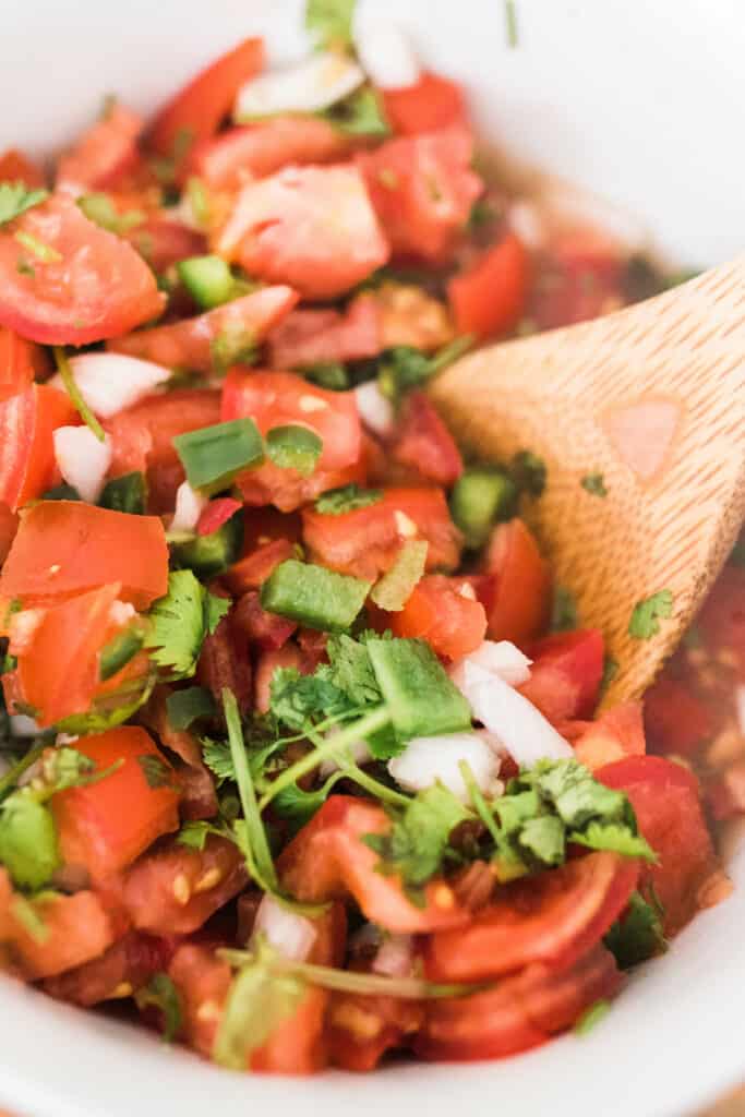 close up of fermented salsa in a white bowl with a wooden spoon