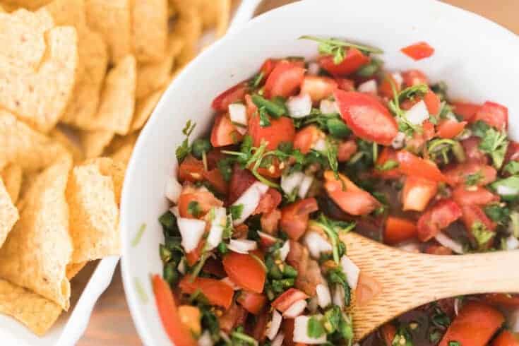 fermented salsa in a white bowl with a wooden spoon surrounded by tortilla chips