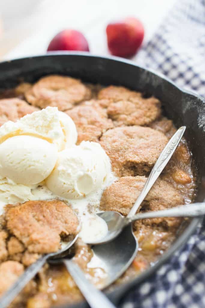 up close picture of sourdough peach cobbler topped with ice cream in a cast iron skillet