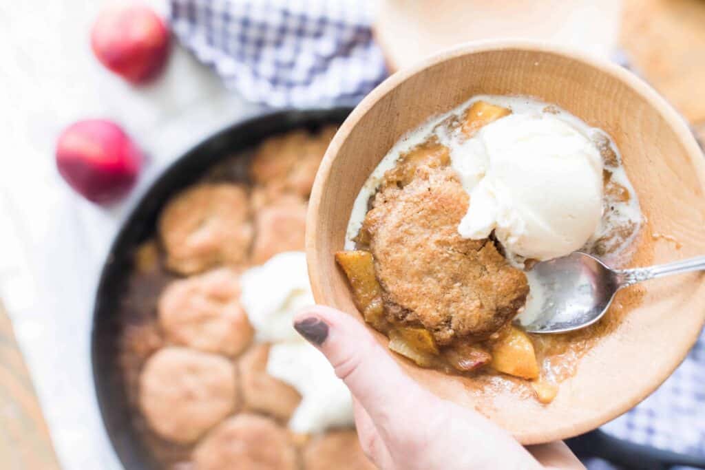 hand holding bowl of sourdough peach cobbler served topped with ice cream