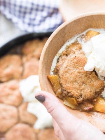hand holding bowl of sourdough peach cobbler served topped with ice cream