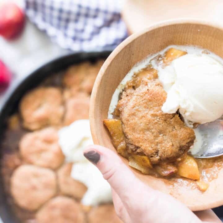 hand holding bowl of sourdough peach cobbler served topped with ice cream