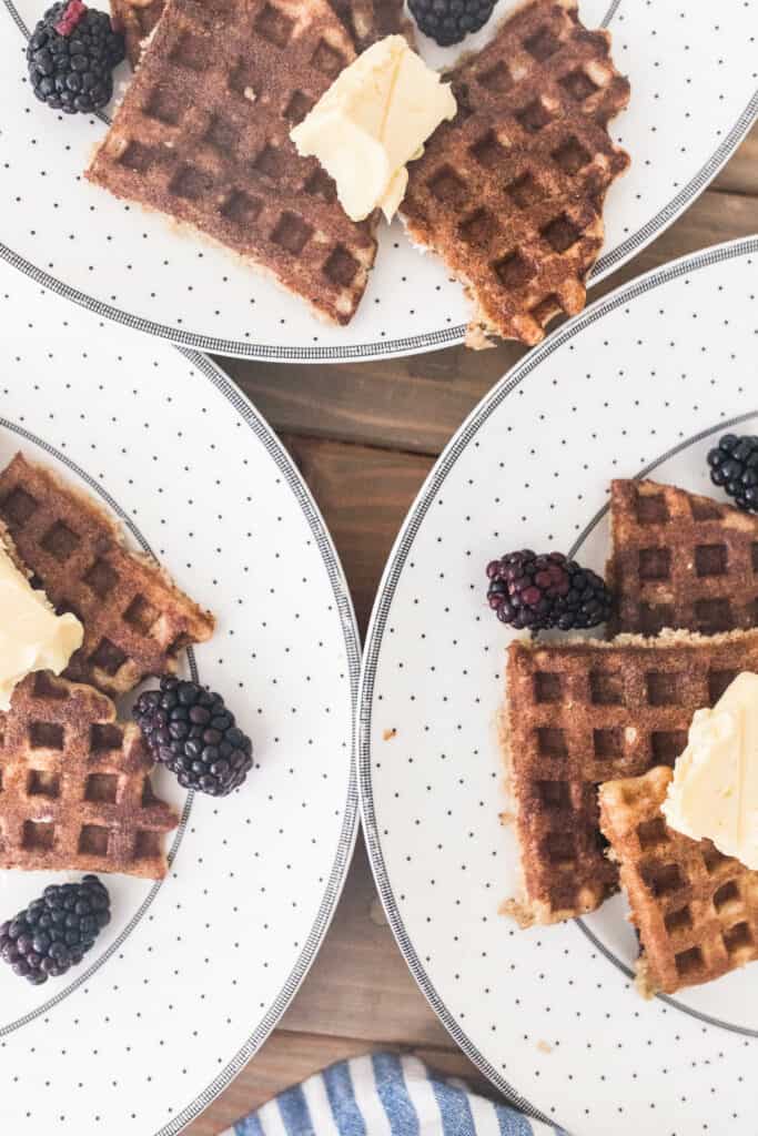 close up shot of crispy sourdough waffles topped with blueberries and butter on white and gray plates