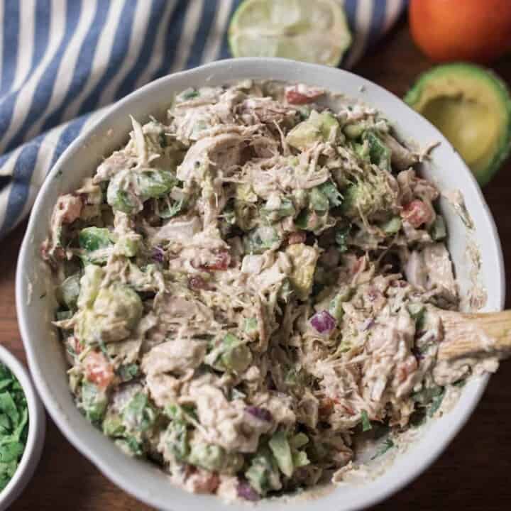 southwest chicken salad in a white bowl with cilantro and avocado around it