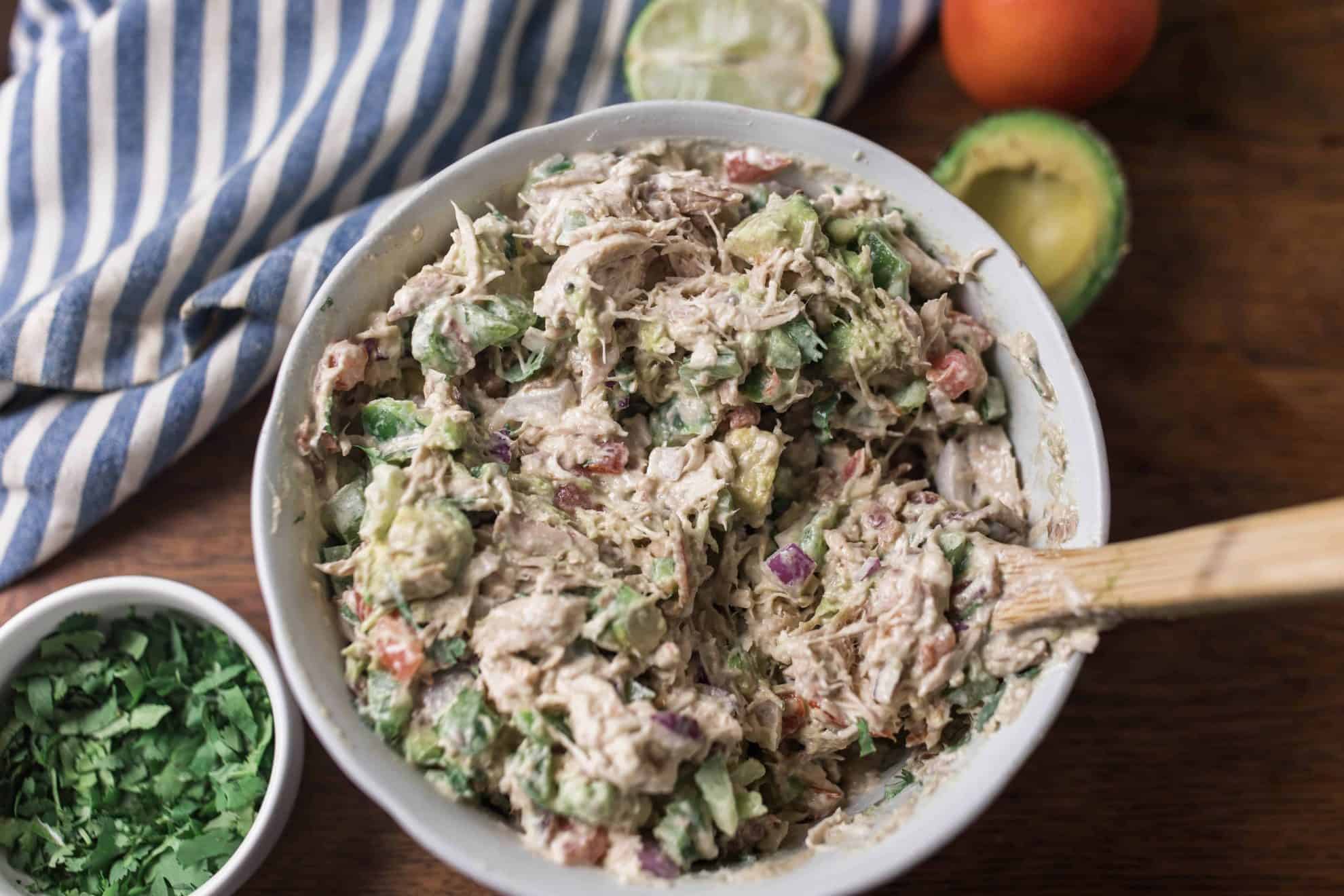 southwest chicken salad in a white bowl with cilantro and avocado around it