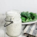 kefir ranch dressing in a vintage mason jar on a striped tea towel with a plate of salad behind it