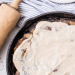 sourdough cinnamon rolls covered in cream cheese topping in a cast iron skillet