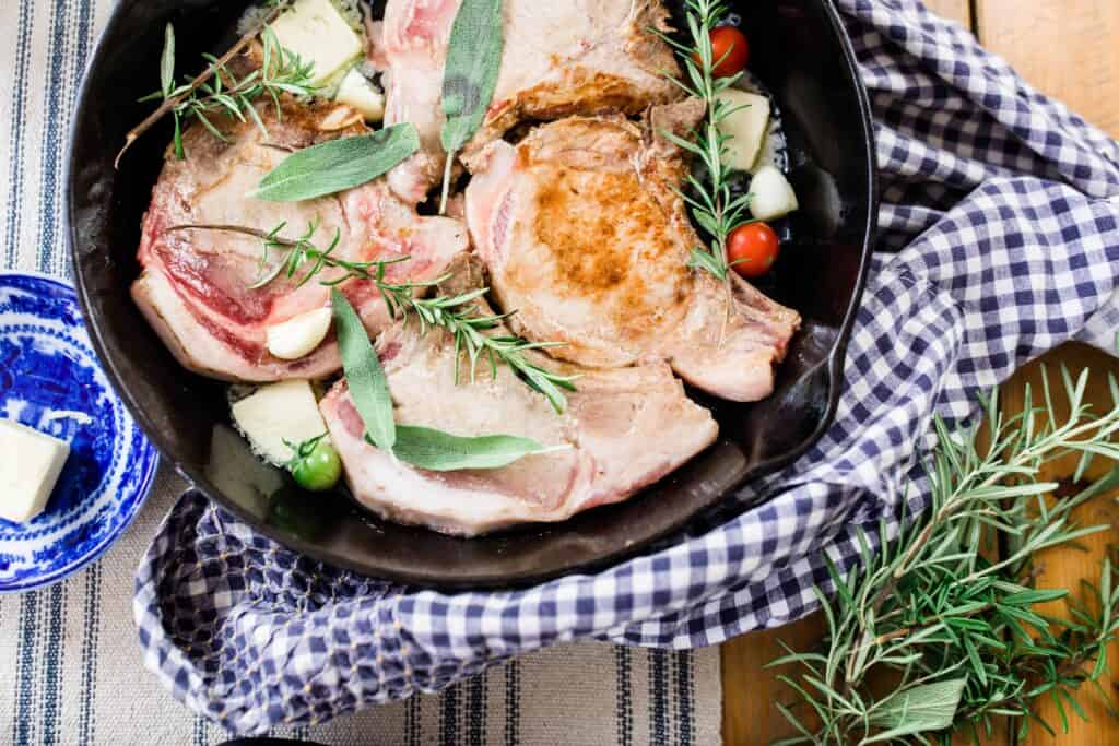 skillet pork chops in a cast iron skillet with fresh herbs on a blue and white towel