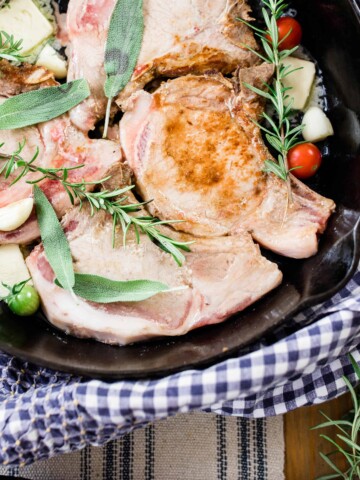 skillet pork chops in a cast iron skillet with fresh herbs on a blue and white towel