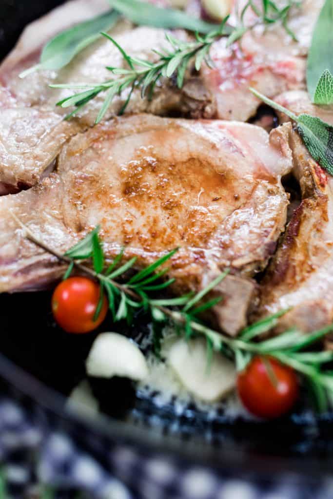 pork chops in a cast iron skillet with rosemary, onions and tomatoes