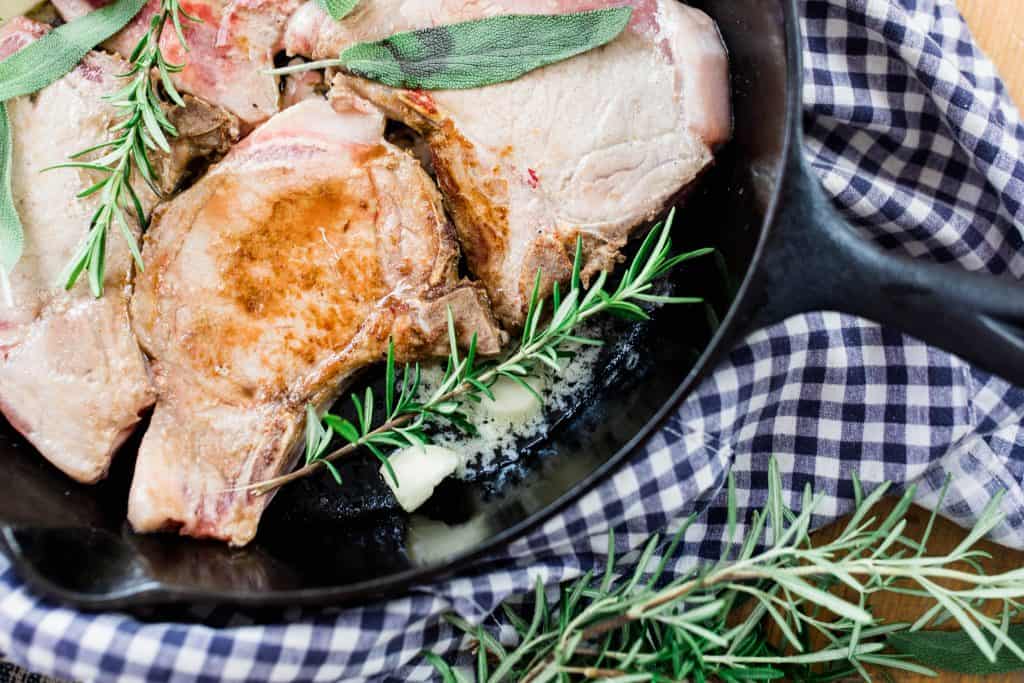 pork chops in a cast iron skillet on top a blue and white napkin