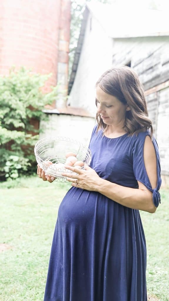 pregnant women wearing a blue dress holding a basket full of farm fresh chicken eggs