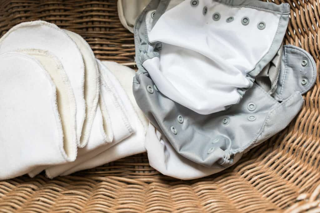 DIY cloth diaper inserts and a gray diaper cover in a wicker laundry basket