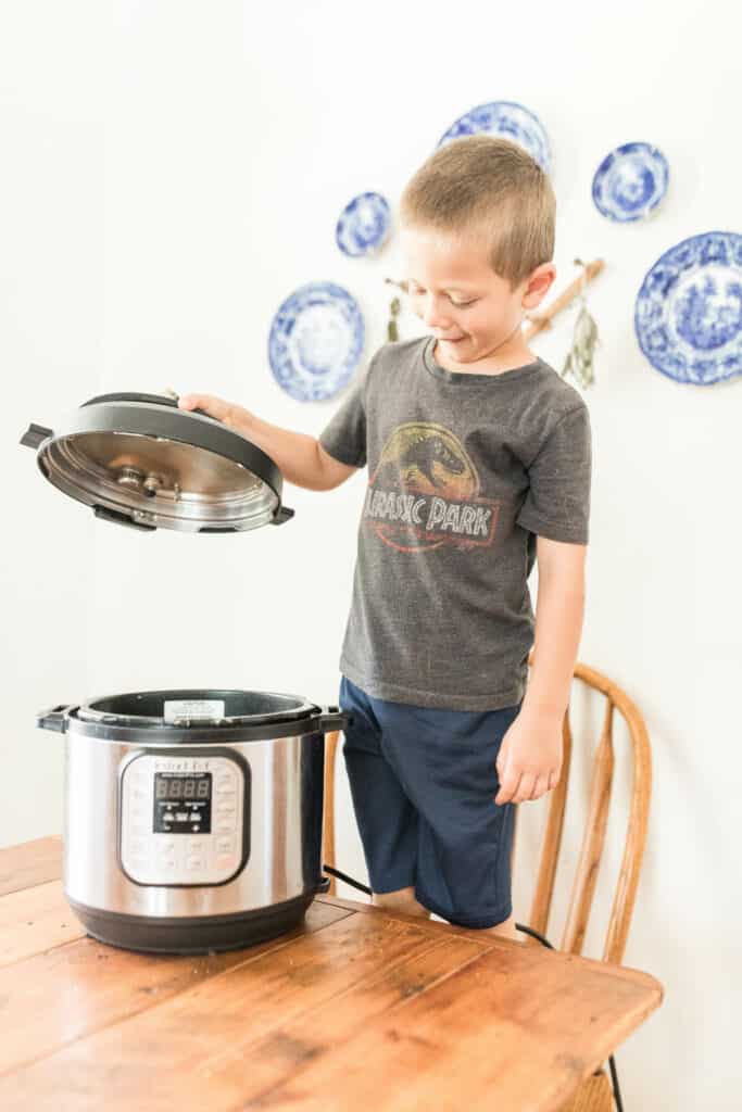 little boy standing on a chair holding the lid to the Instant Pot