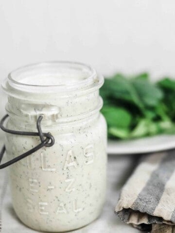 kefir ranch dressing in a vintage mason jar on a striped tea towel with a plate of salad behind it