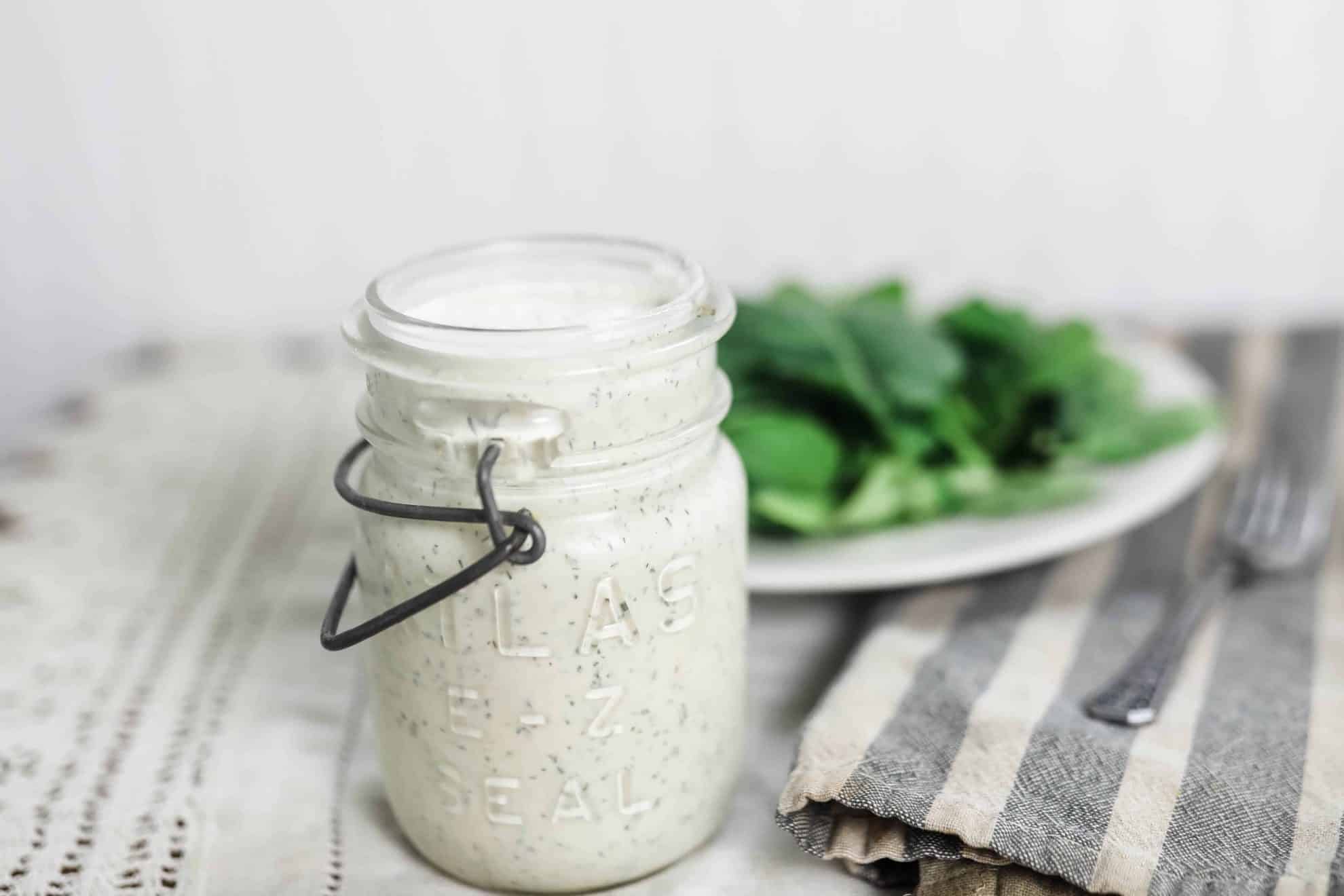 kefir ranch dressing in a vintage mason jar on a striped tea towel with a plate of salad behind it
