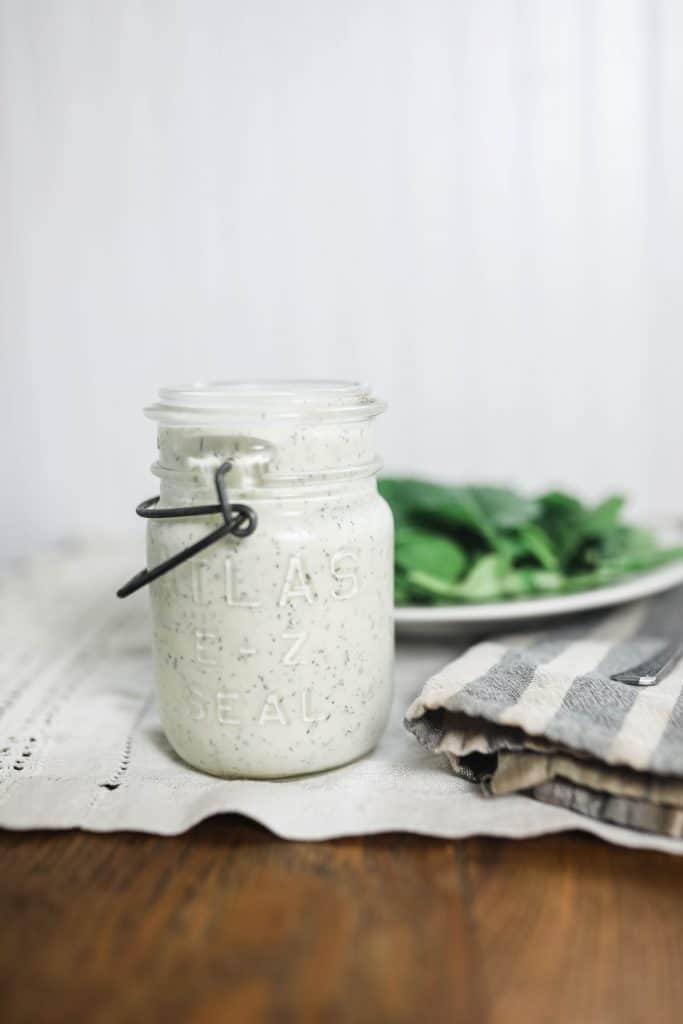 kefir ranch dressing recipe in a vintage mason jar on top of tea towel with greens on a plate behind it