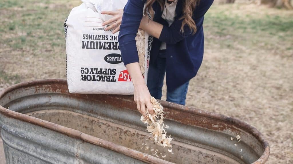 women adding Tractor Supply pine bedding into chicken coop