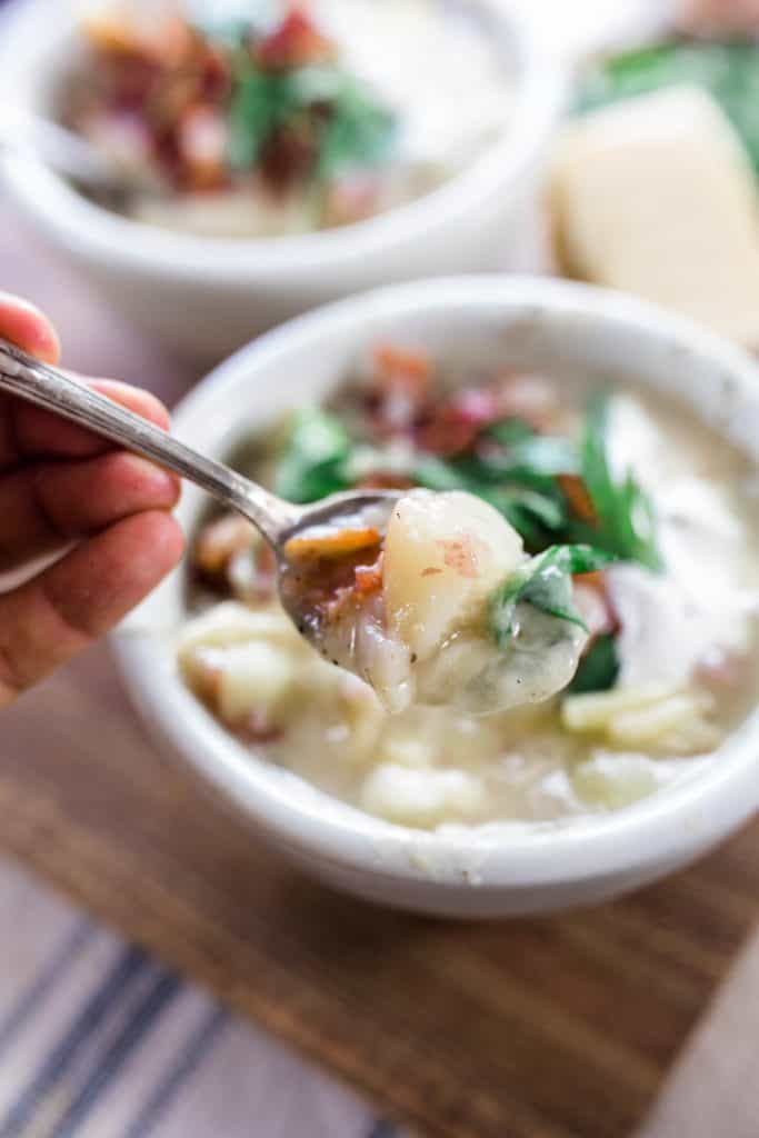 spoonful of healthy potato soup with the bowls of soup in the background