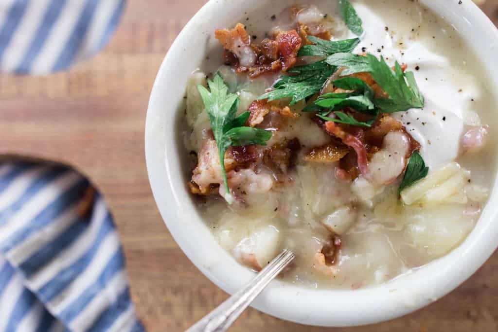 close up picture of potato soup topped with parsley, bacon, cheese and sour cream