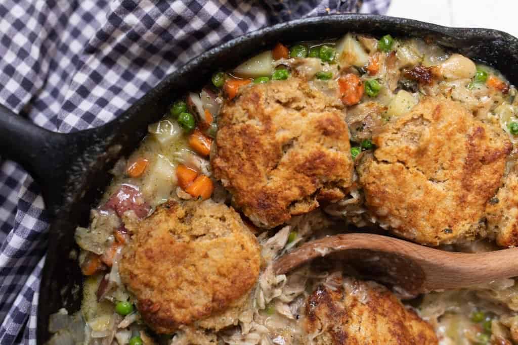 close up picture of the best chicken pot pie in a cast iron skillet. Creamy filling loaded with chicken, potatoes, carrots, and peas are topped with sourdough biscuits and baked to perfection. 