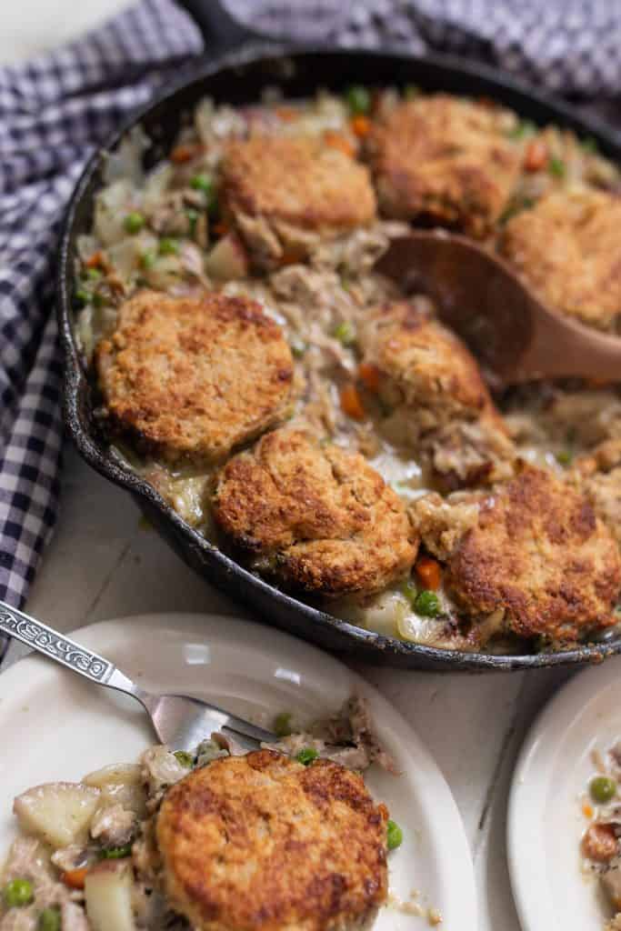 sourdough chicken pot pie in a cast iron skillet with white plates full of chicken pot pie