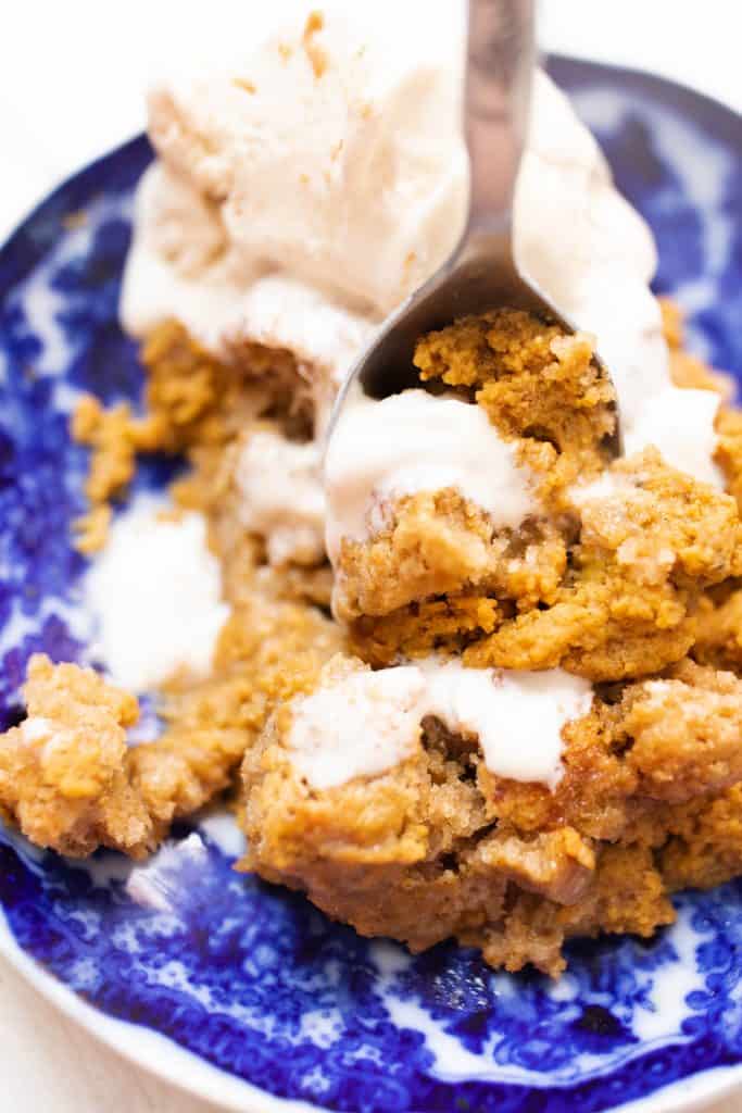 spoon scooping into a blue and white bowl full of spiced sourdough pumpkin cobbler topped with homemade ice cream