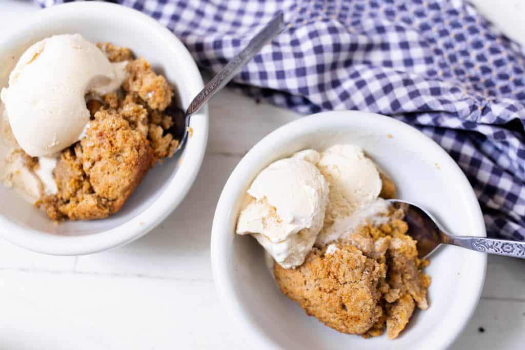 two servings of sourdough pumpkin cobbler in white bowls with a blue and white napkin behind