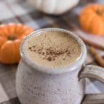 bulletproof pumpkin spice latte topped with pumpkin spice in a stoneware mug with pumpkins behind it