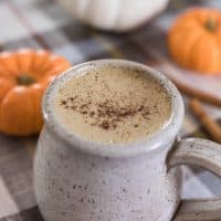 bulletproof pumpkin spice latte topped with pumpkin spice in a stoneware mug with pumpkins behind it