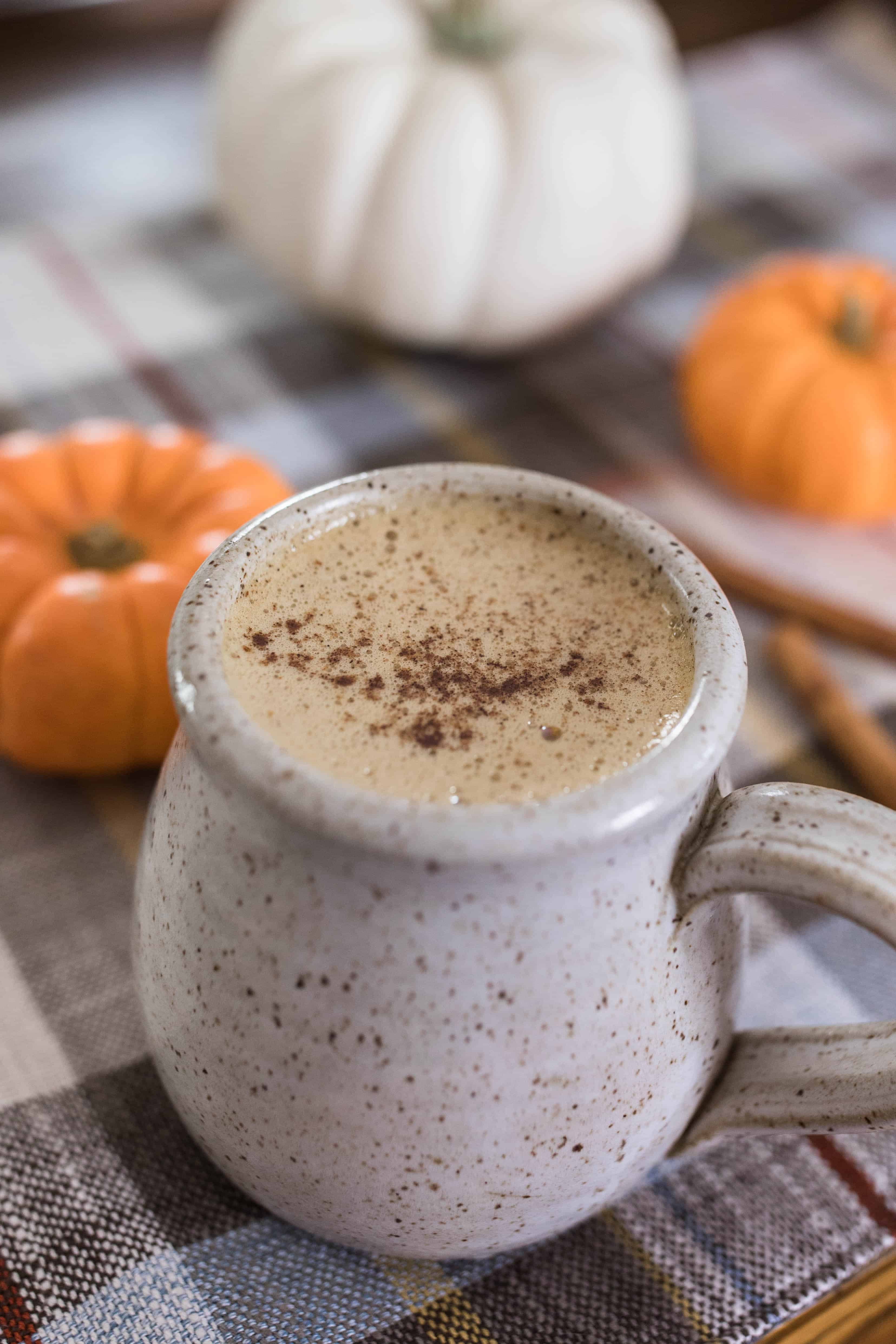 bulletproof pumpkin spice latte topped with pumpkin spice in a stoneware mug with pumpkins behind it