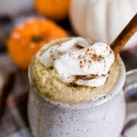 homemade pumpkin spice latte topped with whipped cream and a sprinkle of pumpkin spice in a stoneware mug with pumpkins in the background