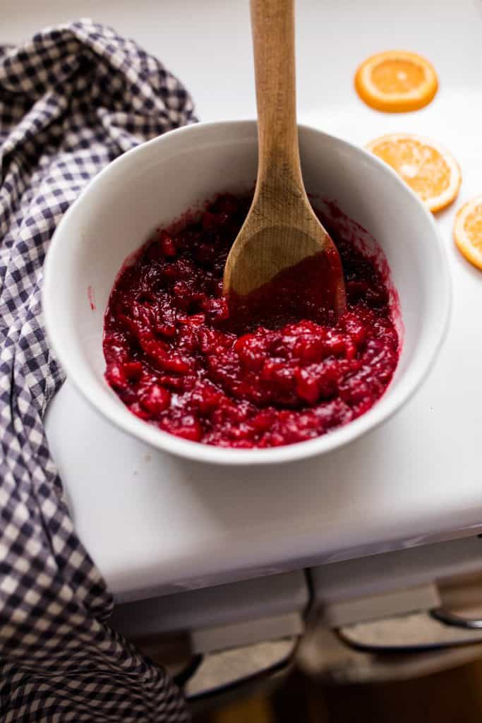cranberry sauce in a white bowl with a wooden spoon in the bowl. Bowl is 