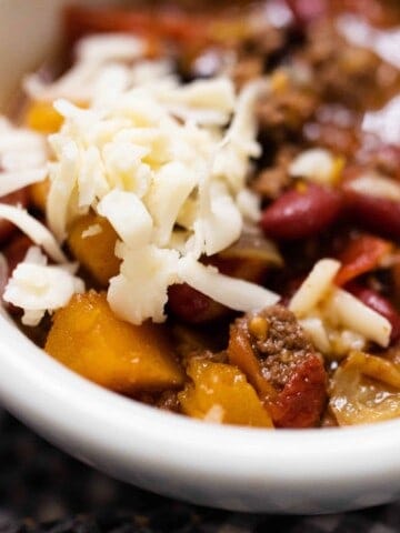 white bowl full of pumpkin chili with ground beef and topped with cheese