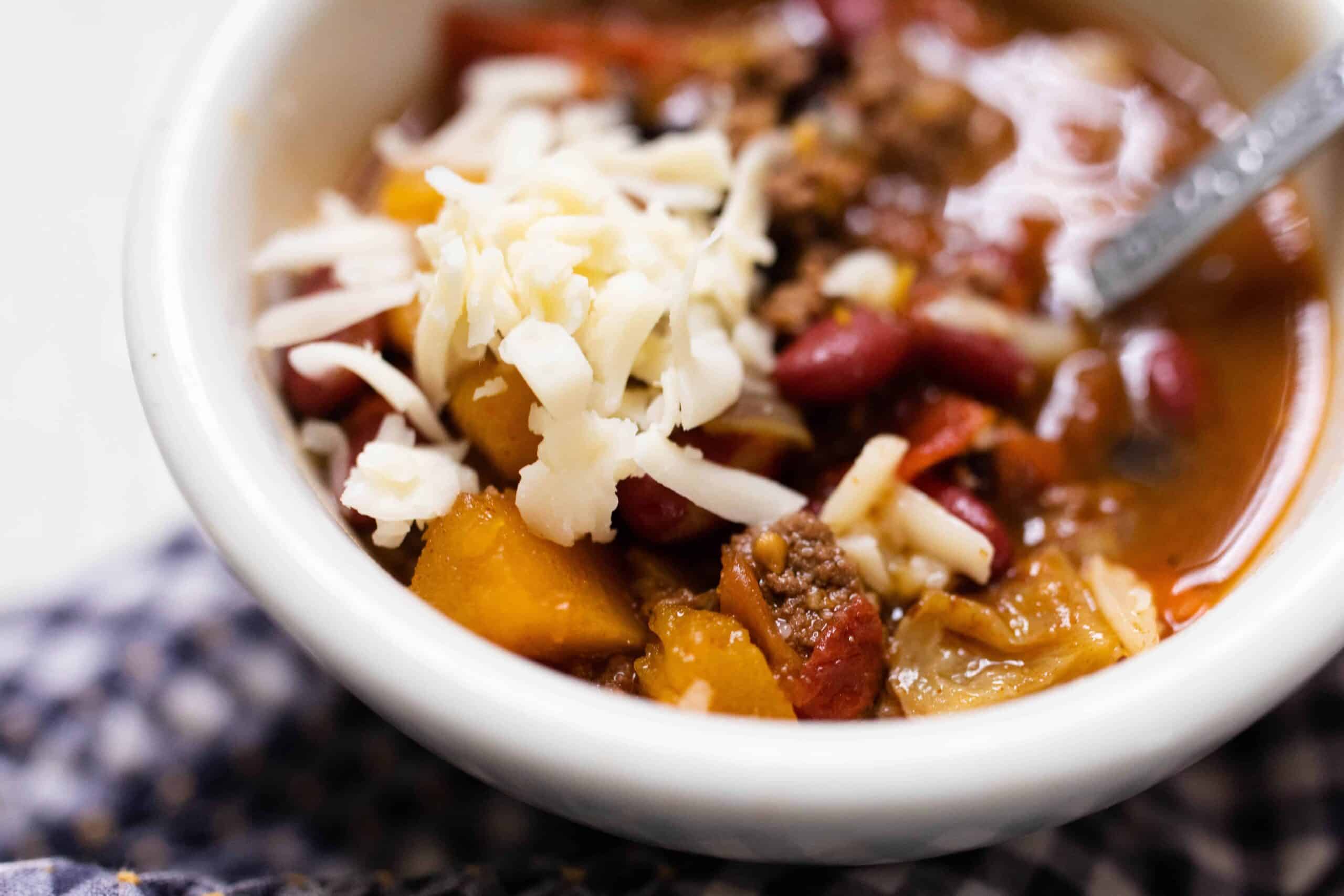 white bowl full of pumpkin chili with ground beef and topped with cheese
