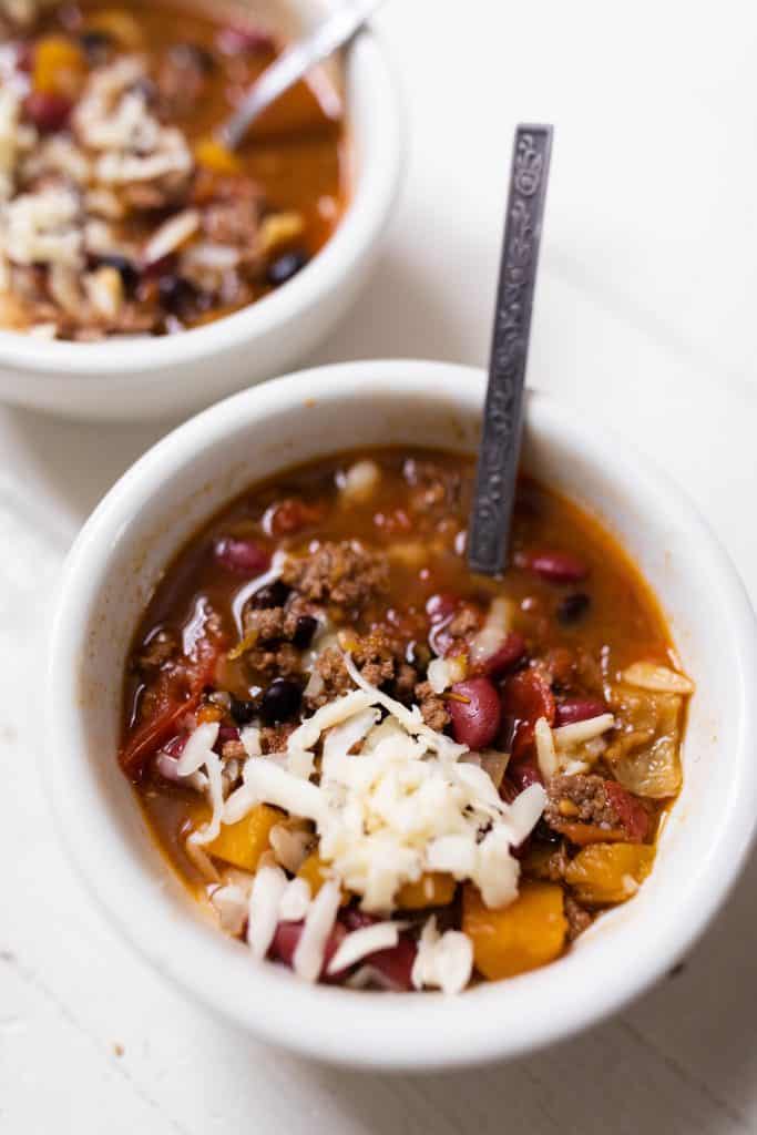 pumpkin chili in a white bowl topped with fresh grated cheese with a spoon in the stew
