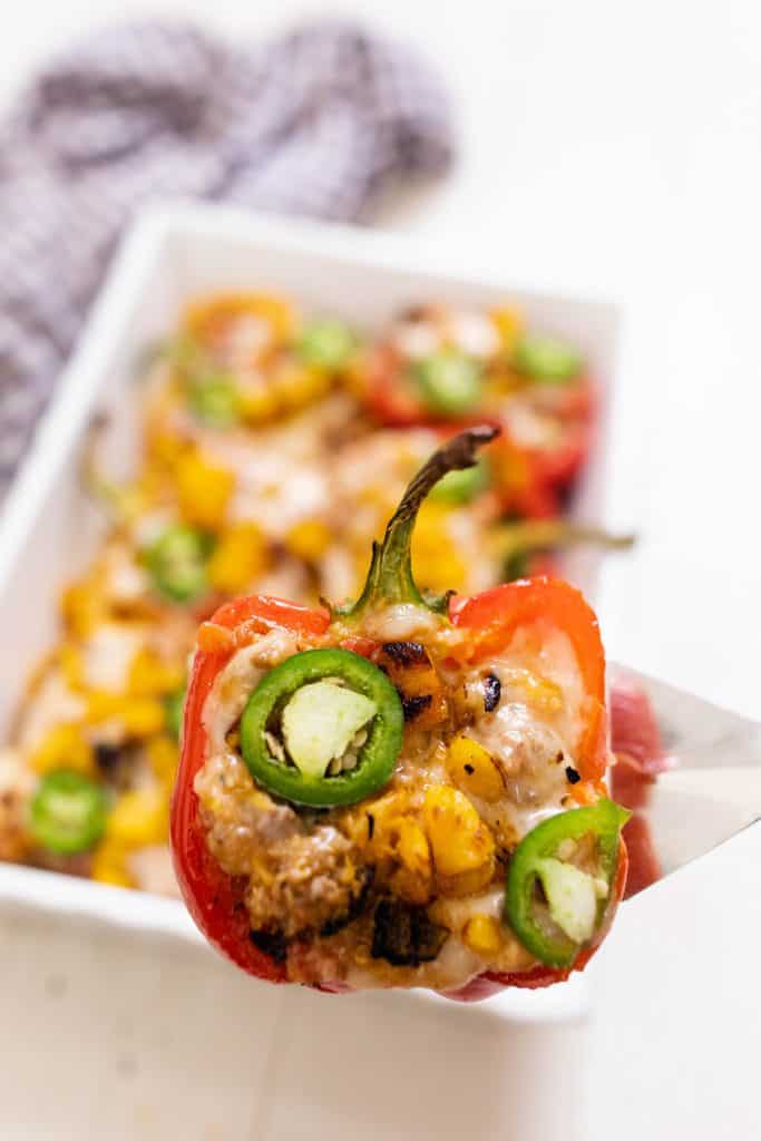 stuffed peppers covered in cheese and sliced jalepenos with a baking dish of peppers behind it.
