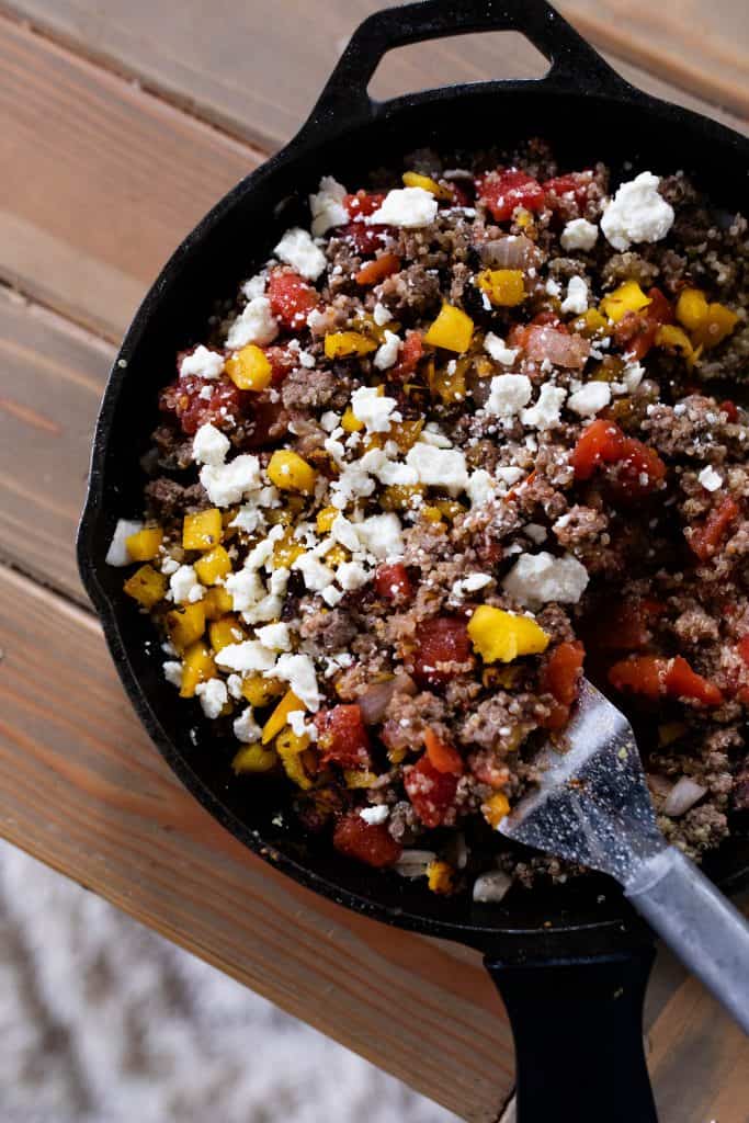 cast iron skillet with ground beef, quinoa, pumpkin, feta cheese, garlic and onions to make stuffed peppers