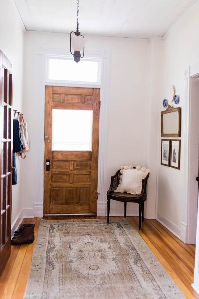 Farmhouse entryway with Victorian features including a original wooden door, turkey rug over beautiful refinished floors, and farmhouse decor