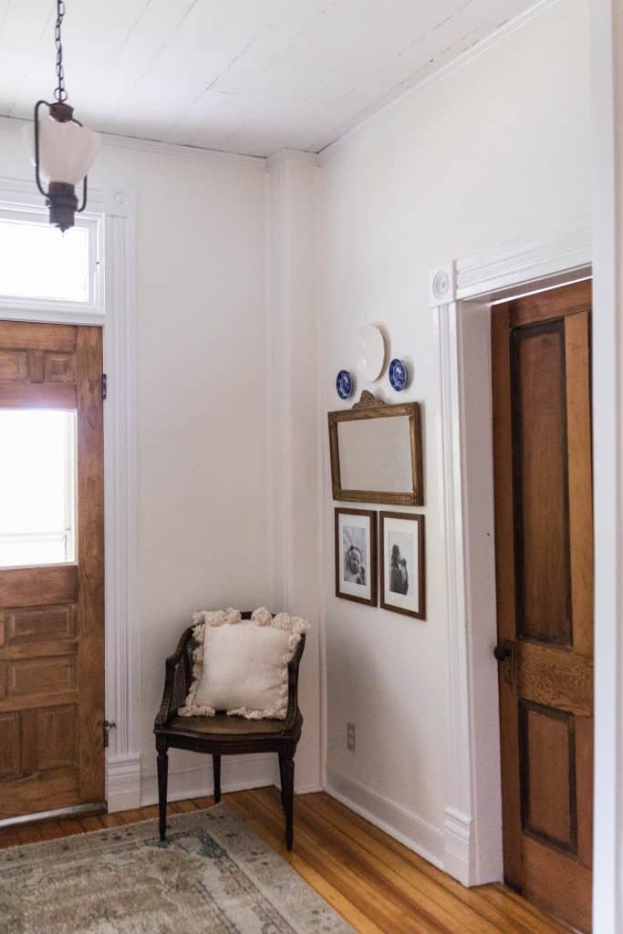 farmhouse entryway - two doors stripped down to the original stain color. Antique lighting hangs above and a chair with wall decor sits in the corner