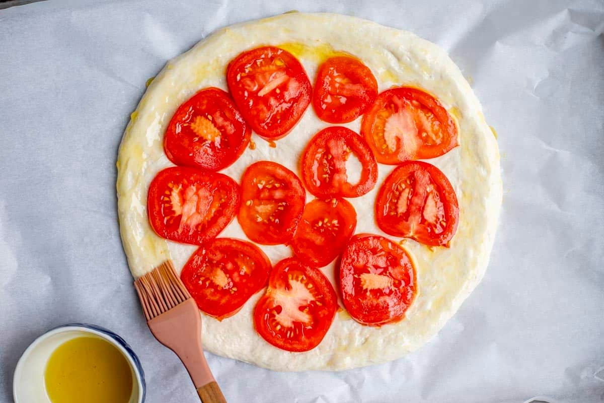 Rolled out pizza dough topped with sliced tomatoes and brushed with olive oil.