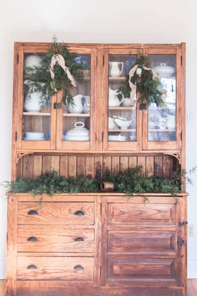 Antique hutch topped with fresh greenery, bells, and candles. Two