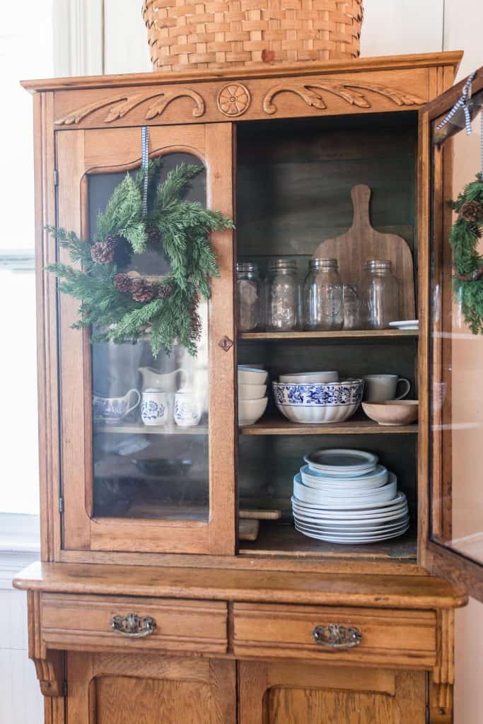 antique wood cabinet with one door open. Greenery wreaths hang off the cabinet doors