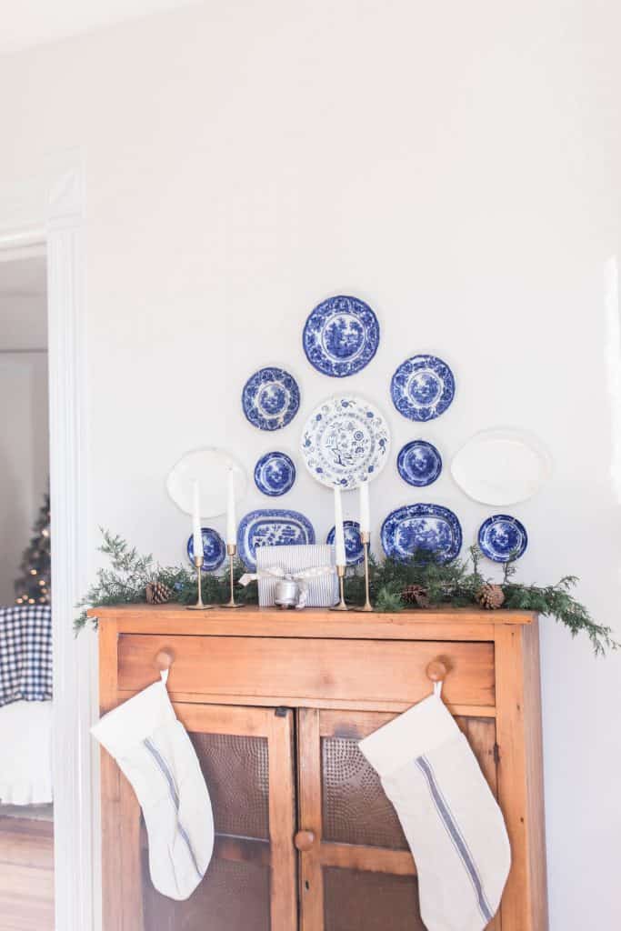 antique pie safe topped with fresh greenery. Antique flow blue plates hang above the pie save. Stocking hang from the knobs of the pie safe