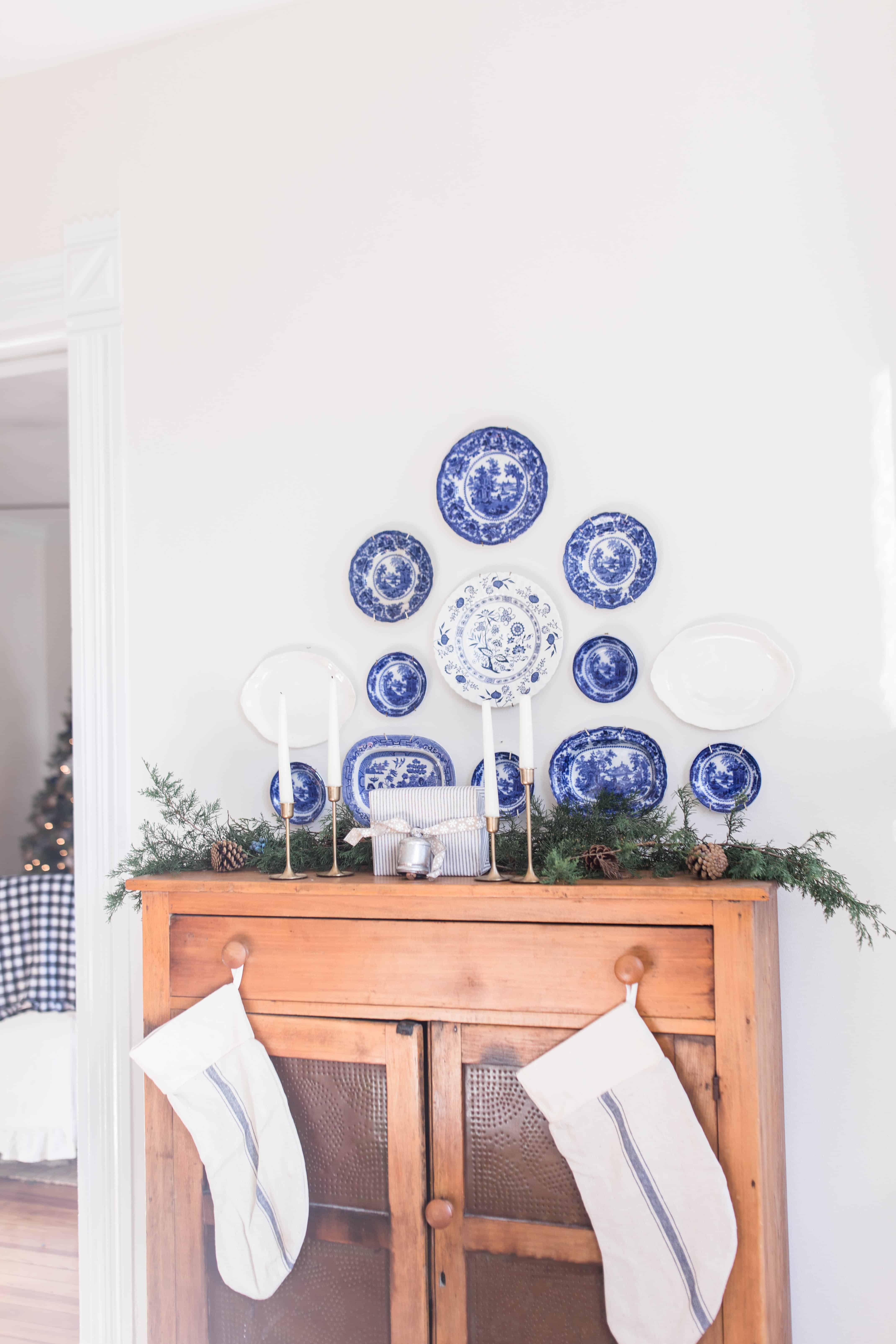 antique pie safe topped with fresh greenery. Antique flow blue plates hang above the pie save. Stocking hang from the knobs of the pie safe